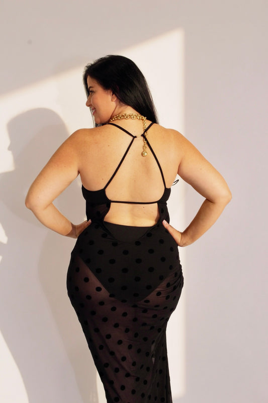 Woman wearing a black polka dot dress with thin straps against a white wall.