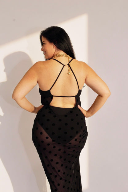 Woman wearing a black polka dot dress with thin straps against a white wall.